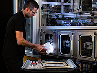 Technician handling materials in front of a large automated industrial machine.