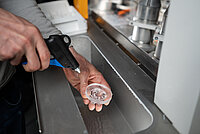 Technician cleaning a processed glass lens with compressed air inside a machine.