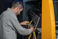 Technician connecting and inspecting cables inside an industrial machine.
