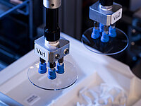 Robotic arm with suction grippers handling a circular glass wafer in a laboratory or manufacturing setting.