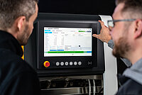 Two technicians reviewing machine data on a touchscreen display.