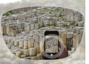 View through a pair of glasses showing stone formations, with a smartphone in the foreground capturing the same scene.