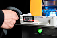 Worker scanning a barcode on a tray with a handheld scanner.