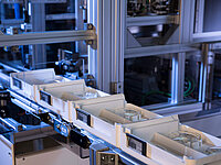 Automated conveyor system transporting trays with components inside a manufacturing facility.