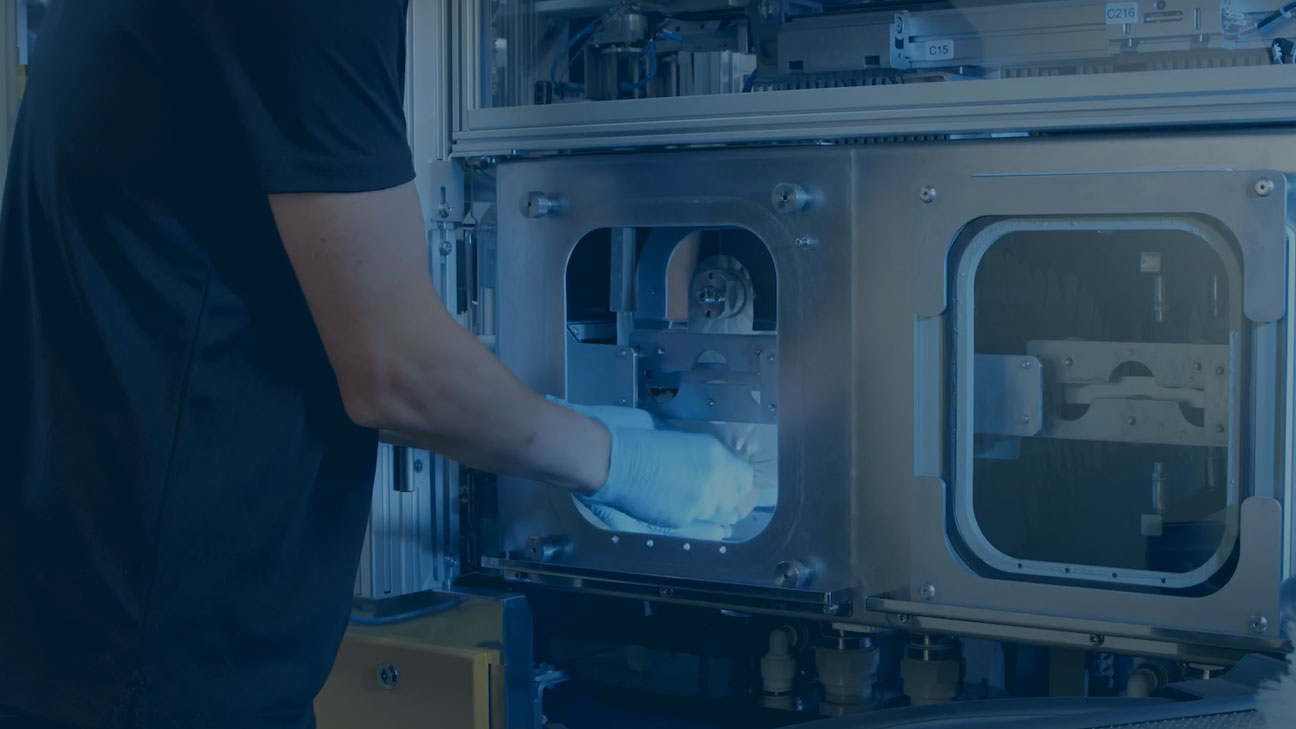 Worker wearing gloves operating a semiconductor manufacturing machine through a front access panel.