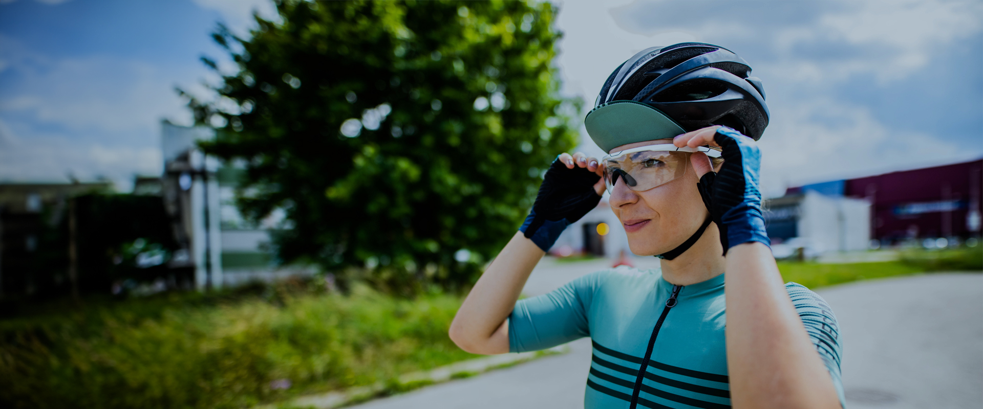 Cyclist wearing a helmet and sportswear, adjusting their glasses outdoors on a sunny day.